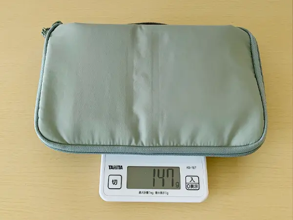 無印良品『コレクションケースA5スリム』の検証写真です。本体の重さを測っている画像です。重さは147グラム。日常のかばんの中の仕分けとして、携帯充電器や手帳などを収納することができます。