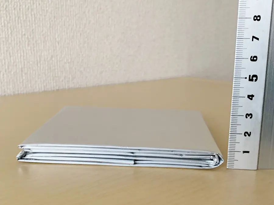 無印良品『エマージェンシーシート』の検証写真です。シートの厚さを隣に定規を立てて、視覚的に見せています。畳んだ状態で厚さが12ミリ程度だということがわかります。