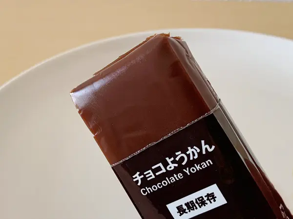 無印良品『備蓄おやつ チョコようかん』の検証写真です。1本単体のイメージ画像です。開け口から三分の一程度開けて、チョコようかんの見えている画像です。見た目は小豆のようかんと同じような、濃い茶色です。